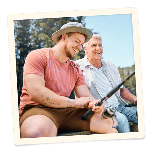A man and his son sitting on a pier, fishing and laughing.